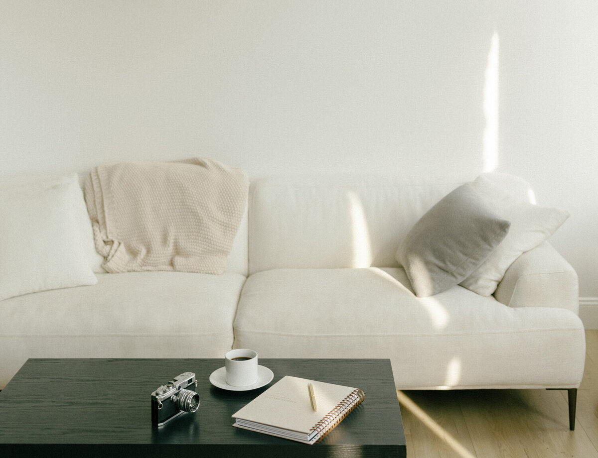 clean white natural light studio with beige linen couch, coffee table, journal