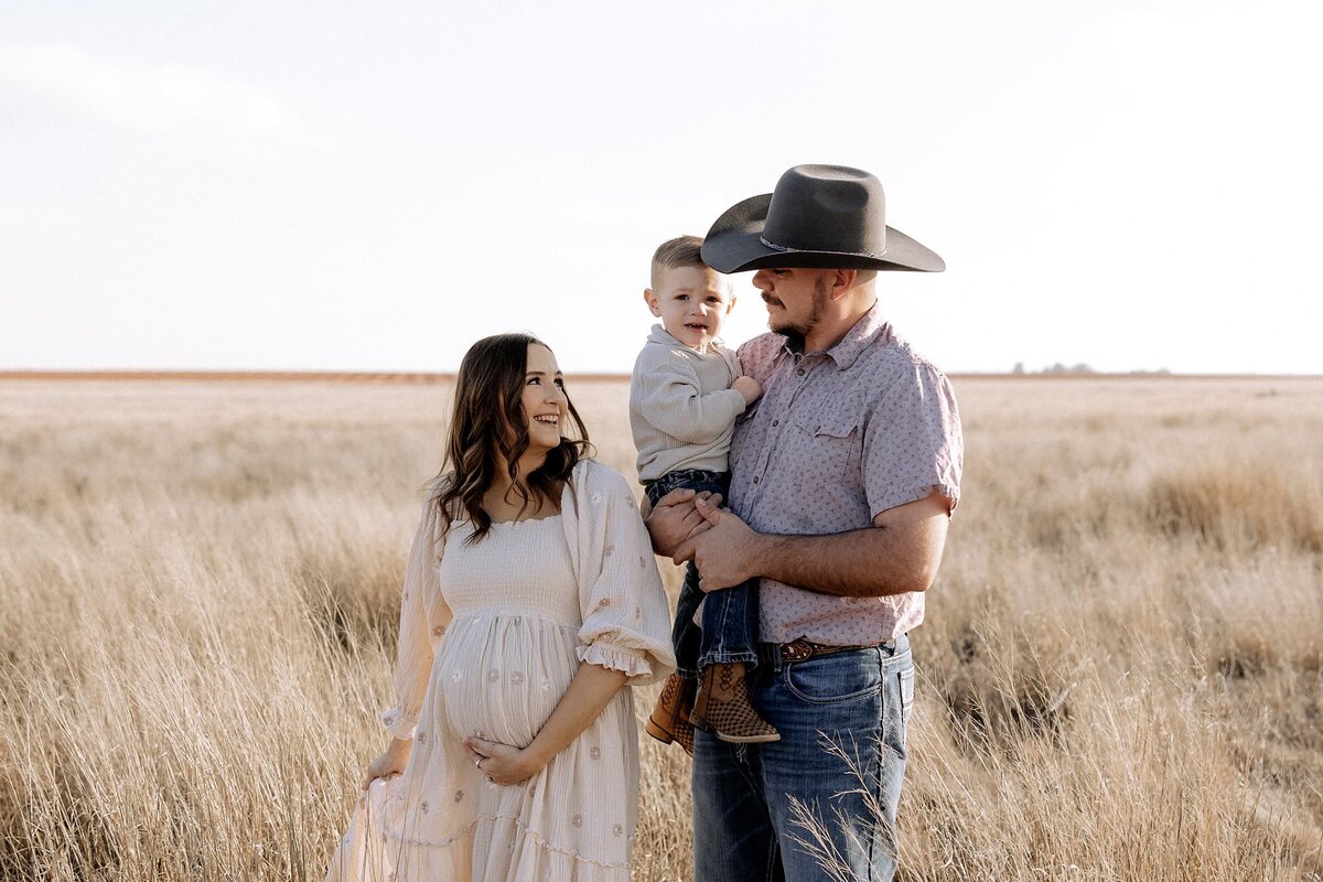 dad holding son and mom holding her belly with her back slightly turned to dad