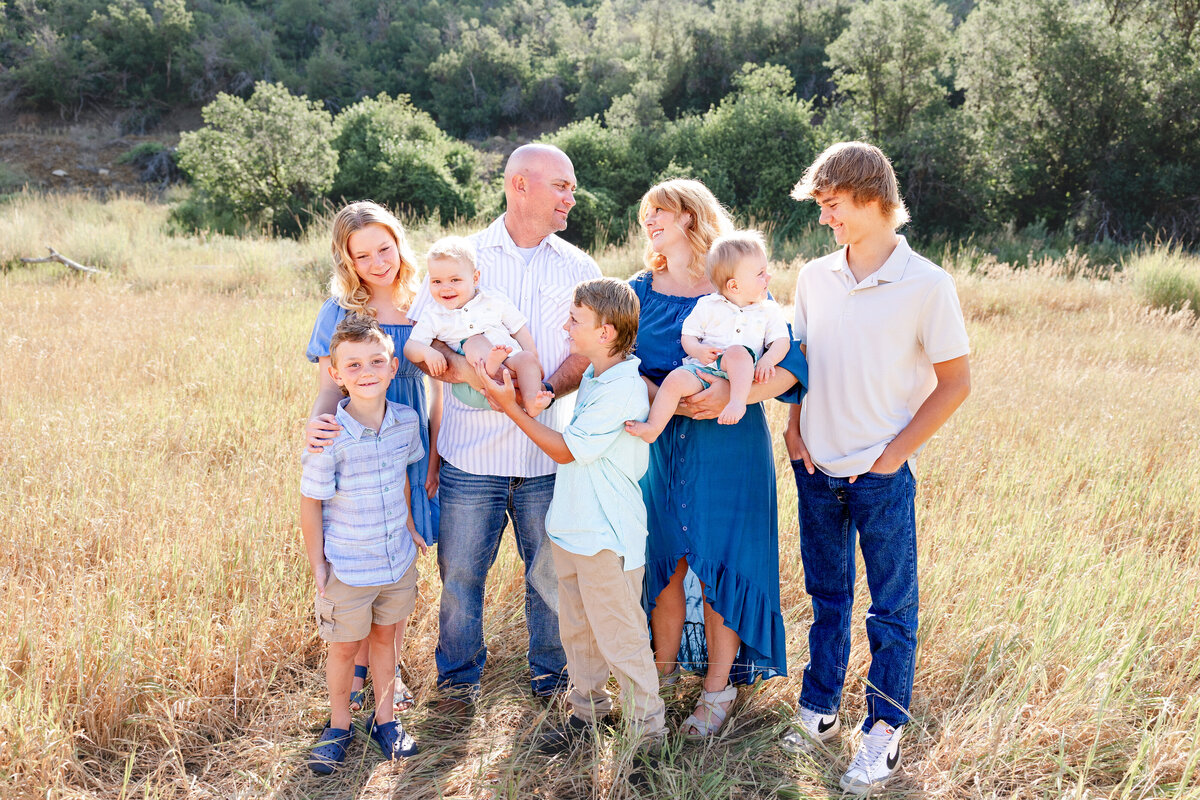 A happy family standing in a sunlit field, smiling and enjoying each other's company during a professional photoshoot