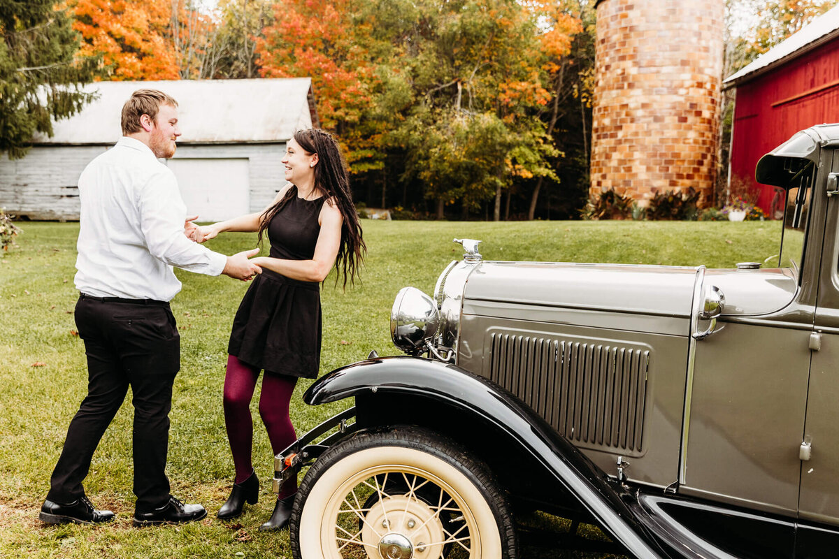 engaged couple dancing by old car by a barn in Green Bay