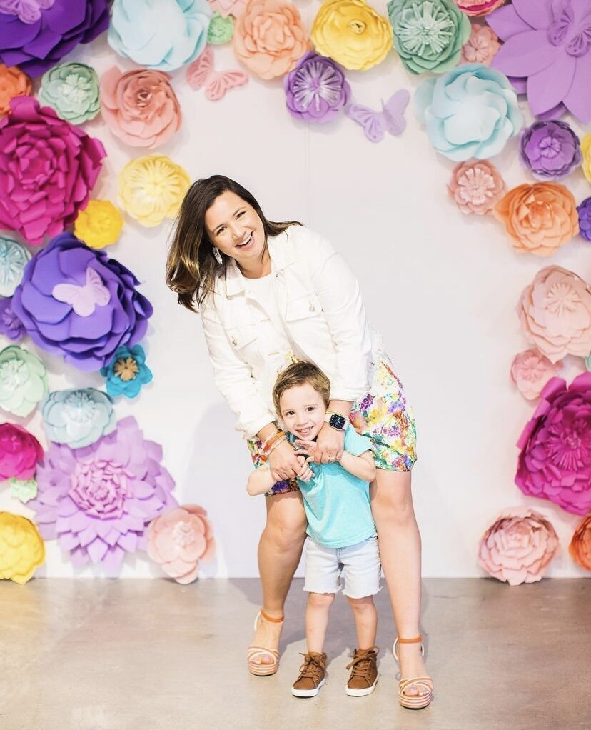 Mother and son posing in front of a white backdrop decorated with large colorful flowers