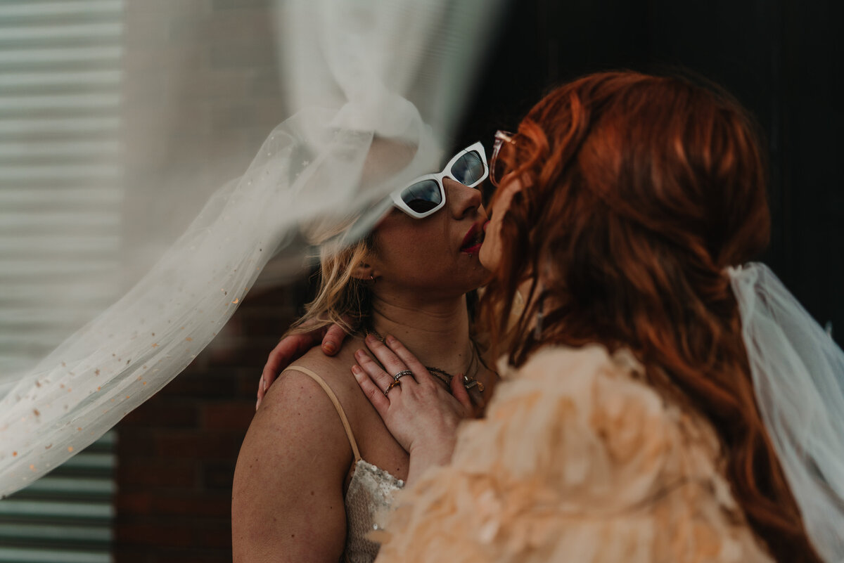 Creative wedding photography shot of two brides kissing under a veil