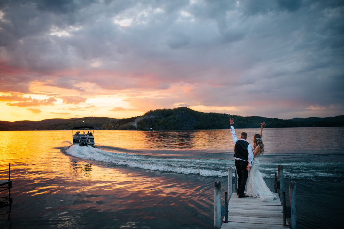 bride and groom waving to boat on dock at sunset wedding lake bomoseen lodge
