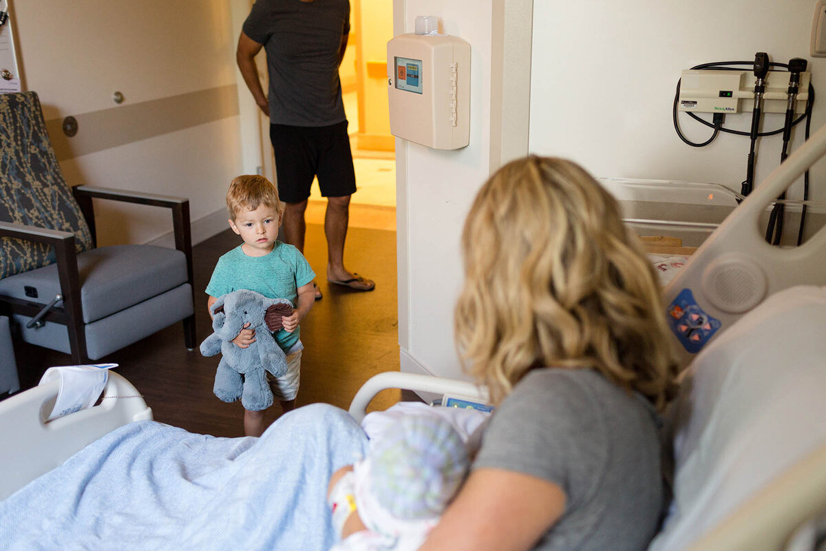 a boy walks into a hospital room to meet his newborn baby brother for the first time