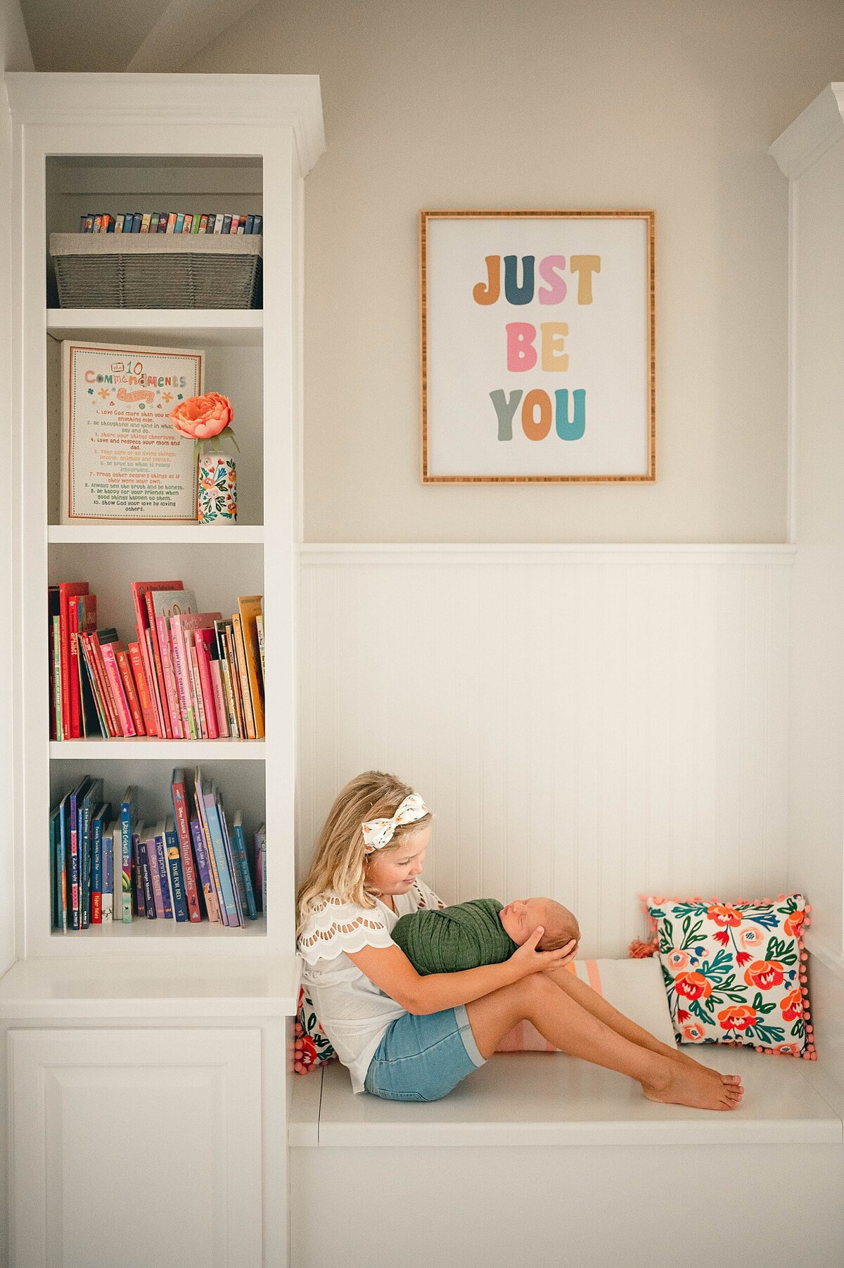 Big sister sitting in reading nook holding baby brother at his Houston Newborn Photography session