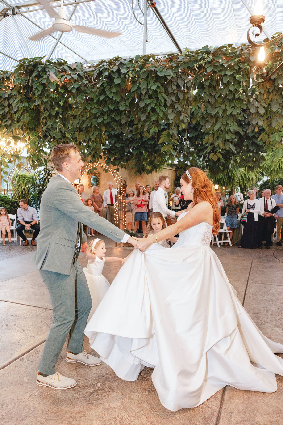 The groom twirls the bride on the dance floor, joined by young flower girls, creating a magical moment at the reception.