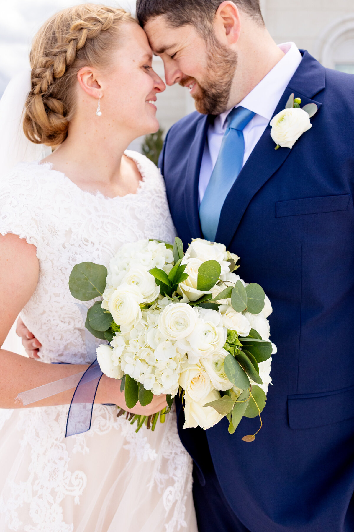 A close-up of the couple sharing an intimate moment, their foreheads touching and smiling with their bouquet in the foreground.