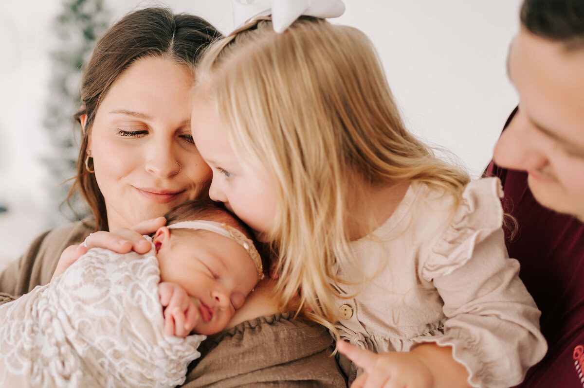 toddler kissing sleeping baby on moms shoulder during Springfield MO newborn photography session