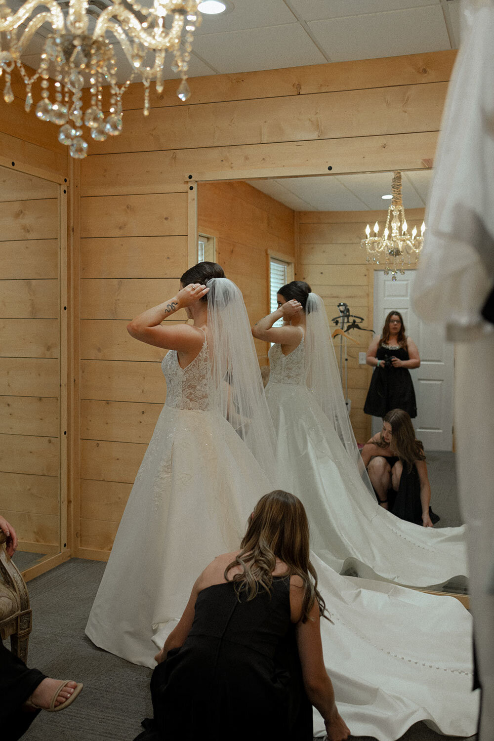 Bride adjusting her veil in front of a mirror, with bridesmaids assisting