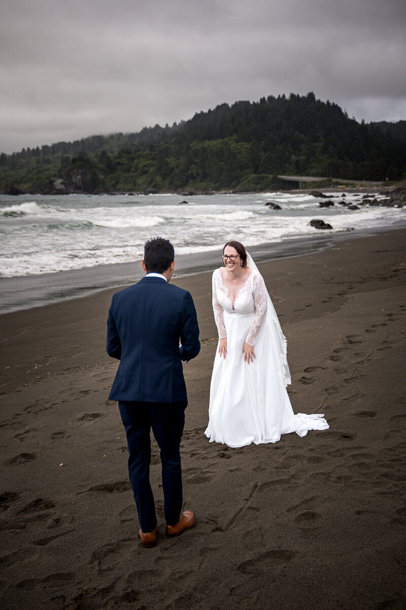 A romantic and candid moment as the groom takes photos of his new bride on the beach in Del Norte County, capturing the love and adventure of their wedding day along the Northern California coast.