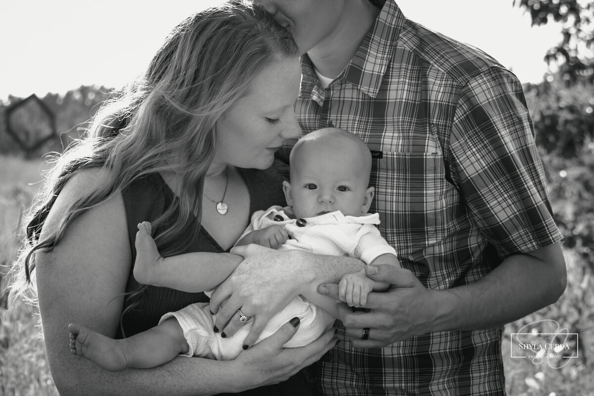 Baby boy looking at camera while mom snuggles close