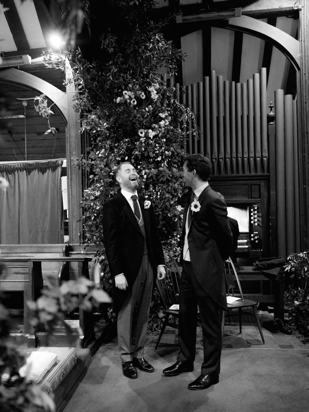 Groom and groomsman laugh at wedding ceremony