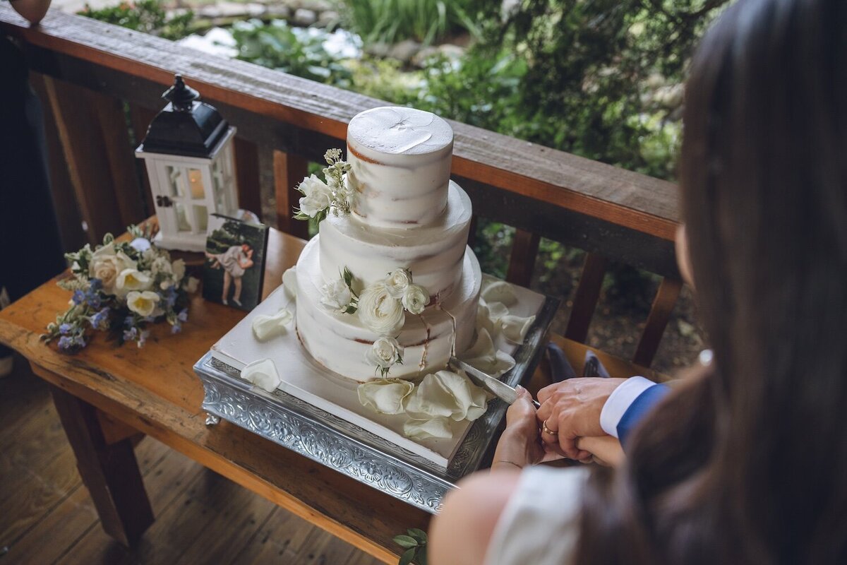 Bride and groom cutting simple white wedding cake with floral accents