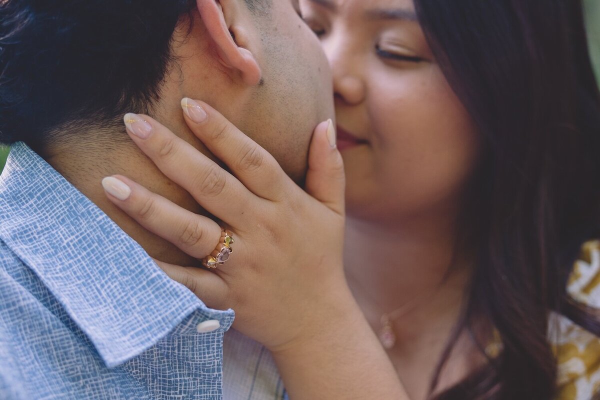 Close-up of bride-to-be smiling with her engagement ring resting on groom-to-be’s face.