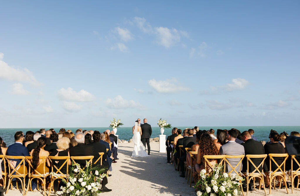 A stunning scene of the bride and groom at the altar, surrounded by guests with the ocean stretching behind them. Florida Keys wedding photography by Claudia Amalia Photography.