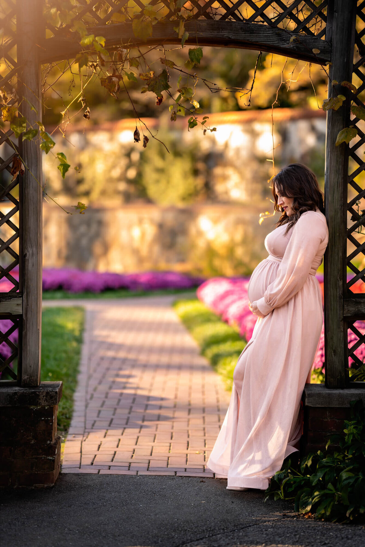 A pregnant woman in a pink dress cradles her bump