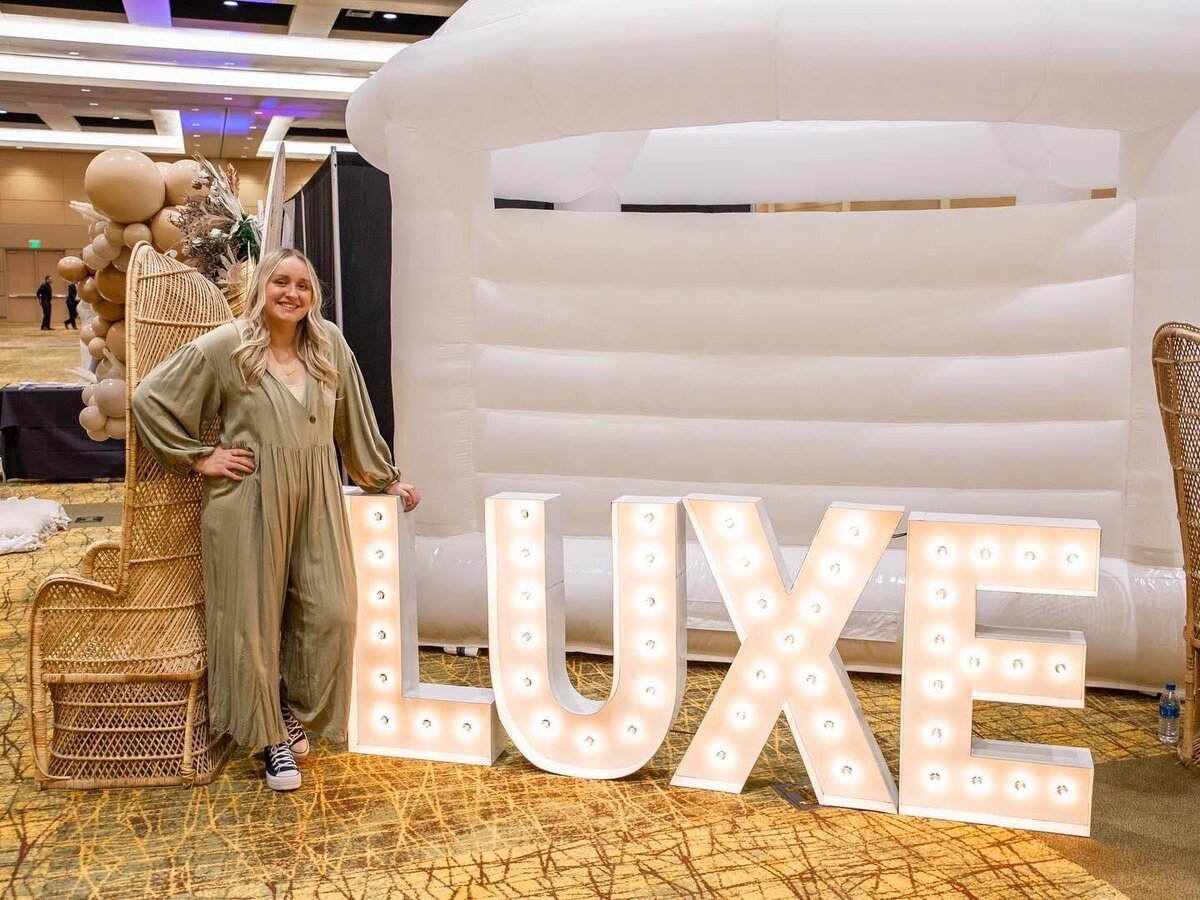 A woman standing next to giant light up marquee letters that spell LUXE.