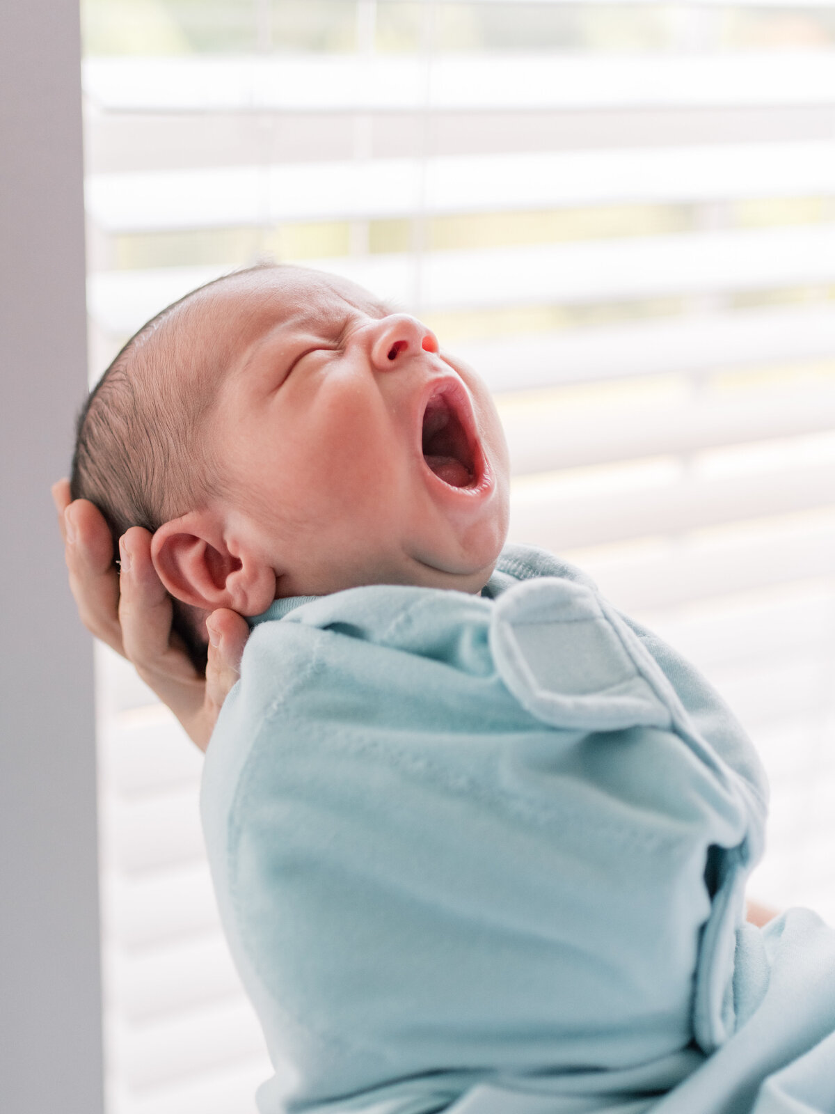 Baby boy wrapped in blue swaddle and yawning.