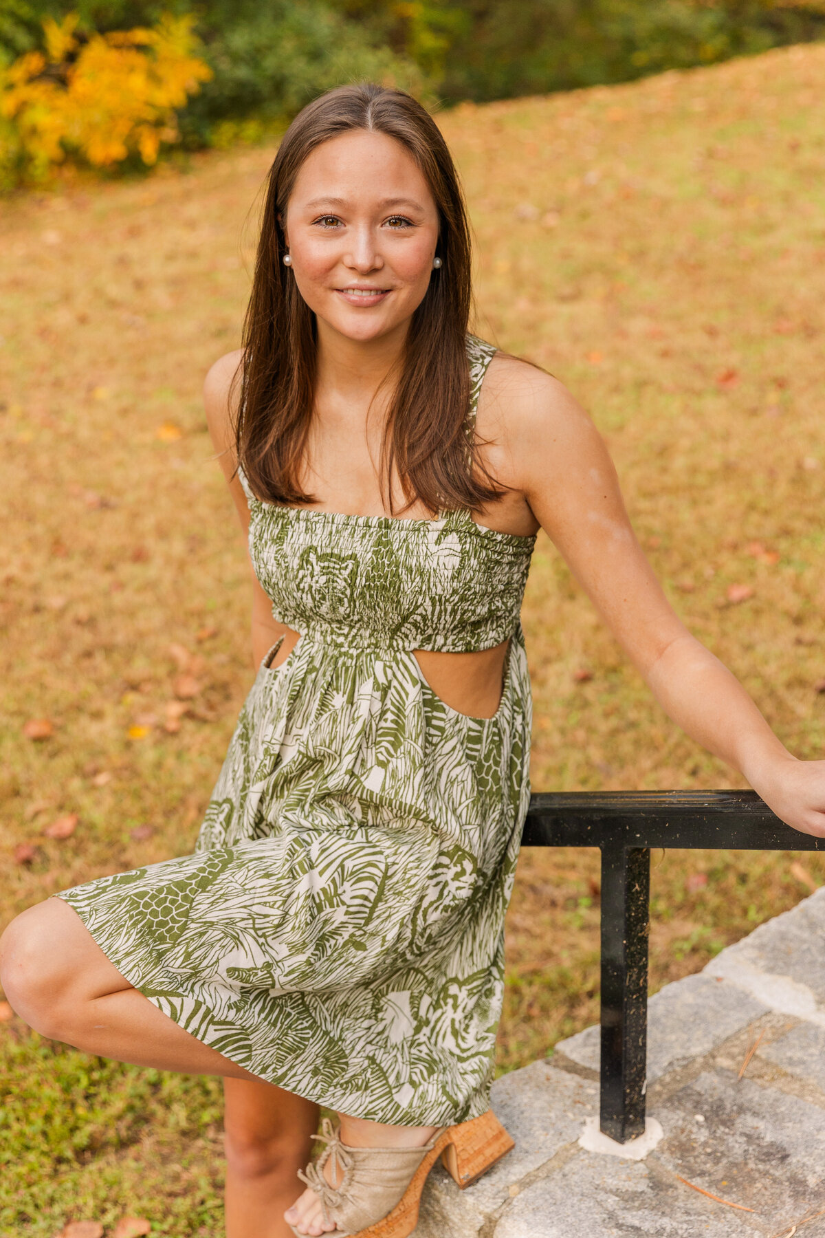 senior girl in green and white pattern dress leaning her back on a handrail looking up at the camera