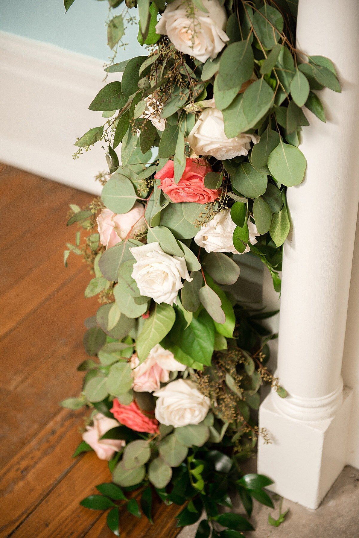 A lush garland of greenery accented with blush, white, ivory and peach roses and flowers hanging down from the ivory mantle in the front blue room at Ravenswood Mansion