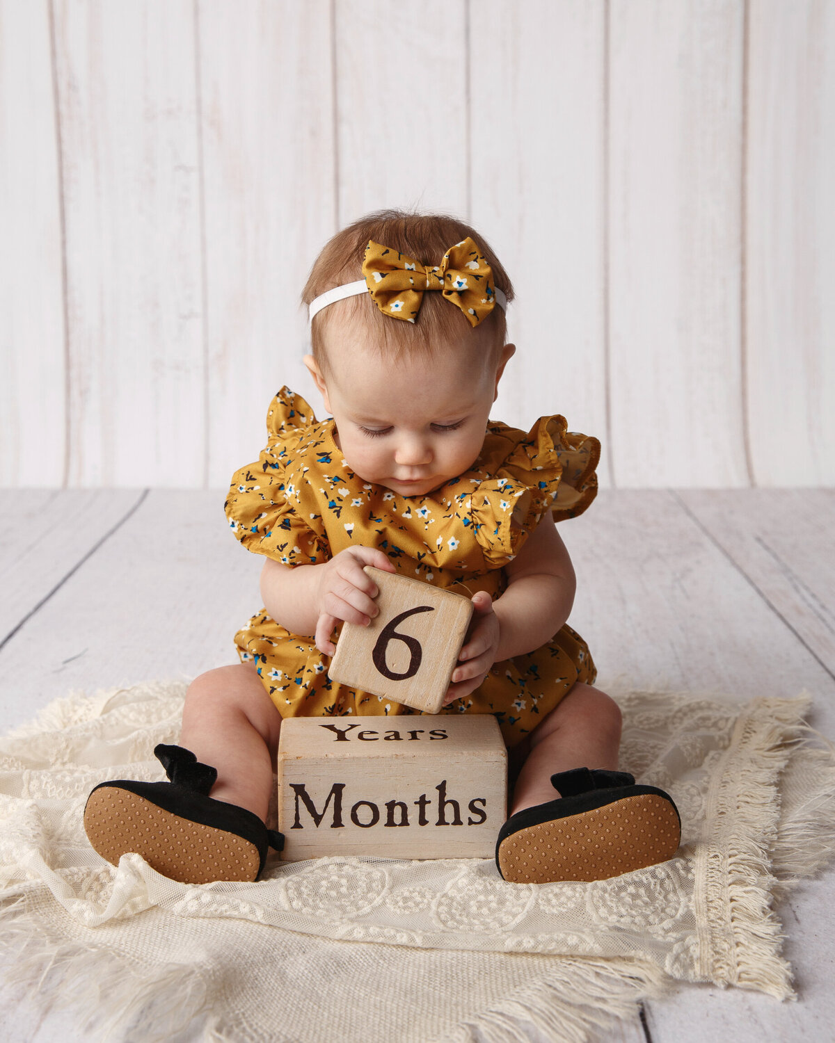 Milestone portrait of a little 6 month old girl wearing a yellow print dress with blocks that spell out her age.