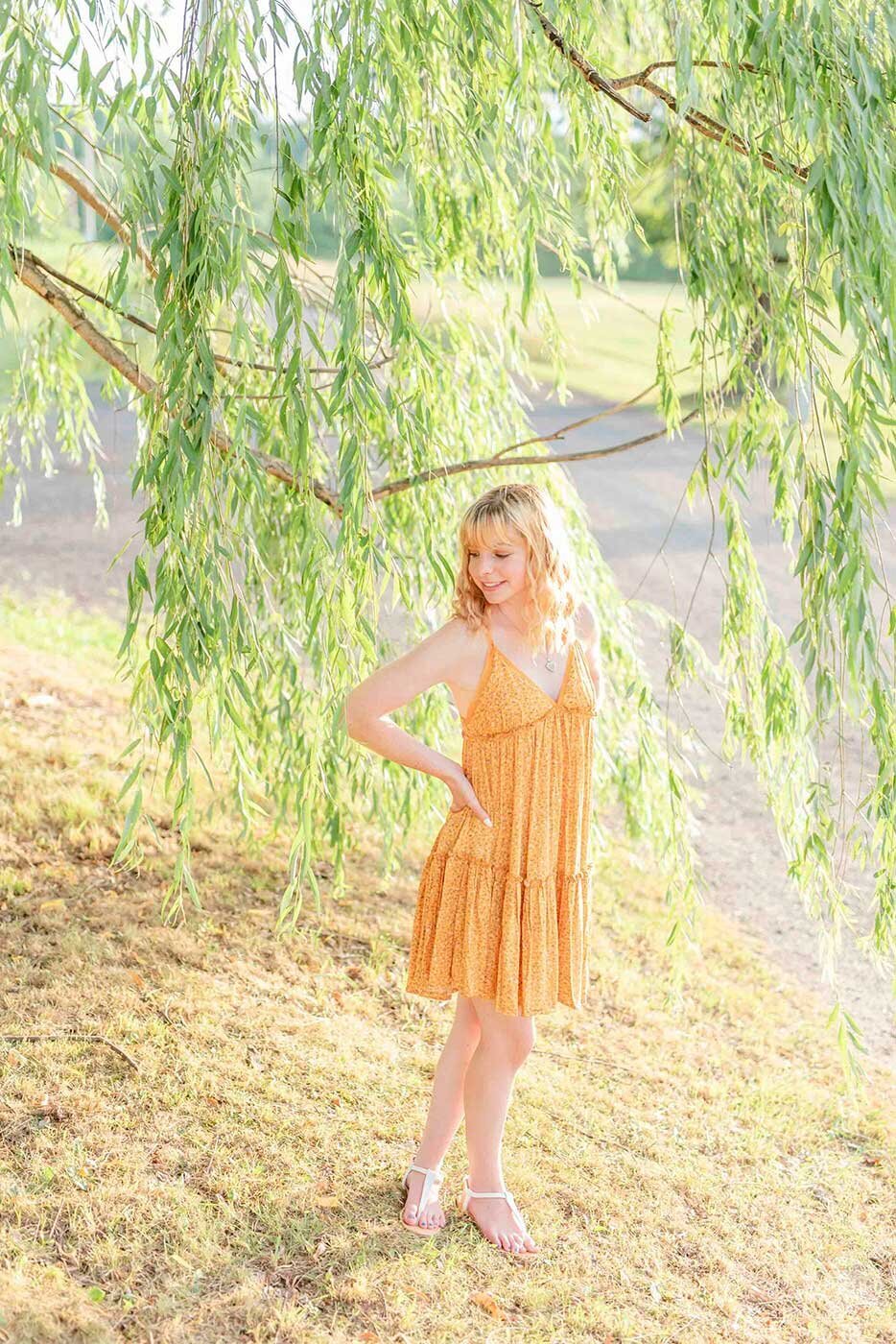 Girl in orange sun dress under weeping willow tree