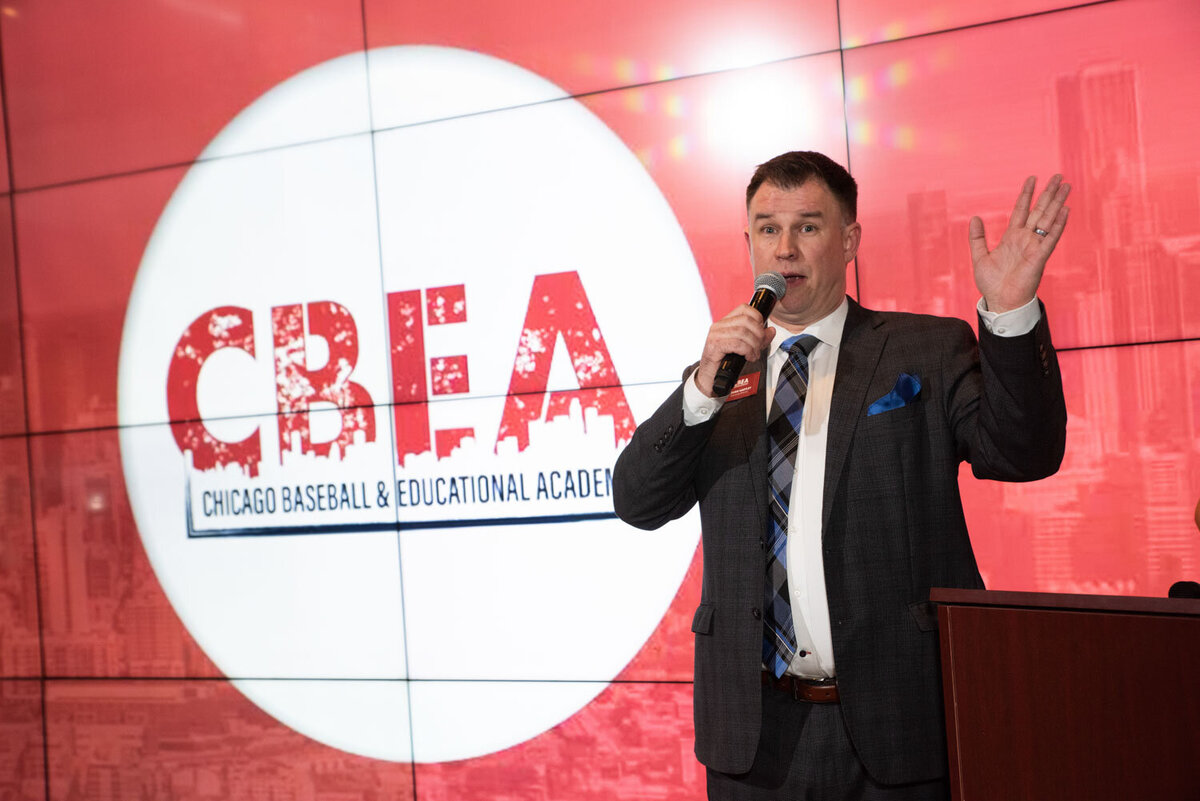 Man in suite and tie speaking in front of CBEA sign