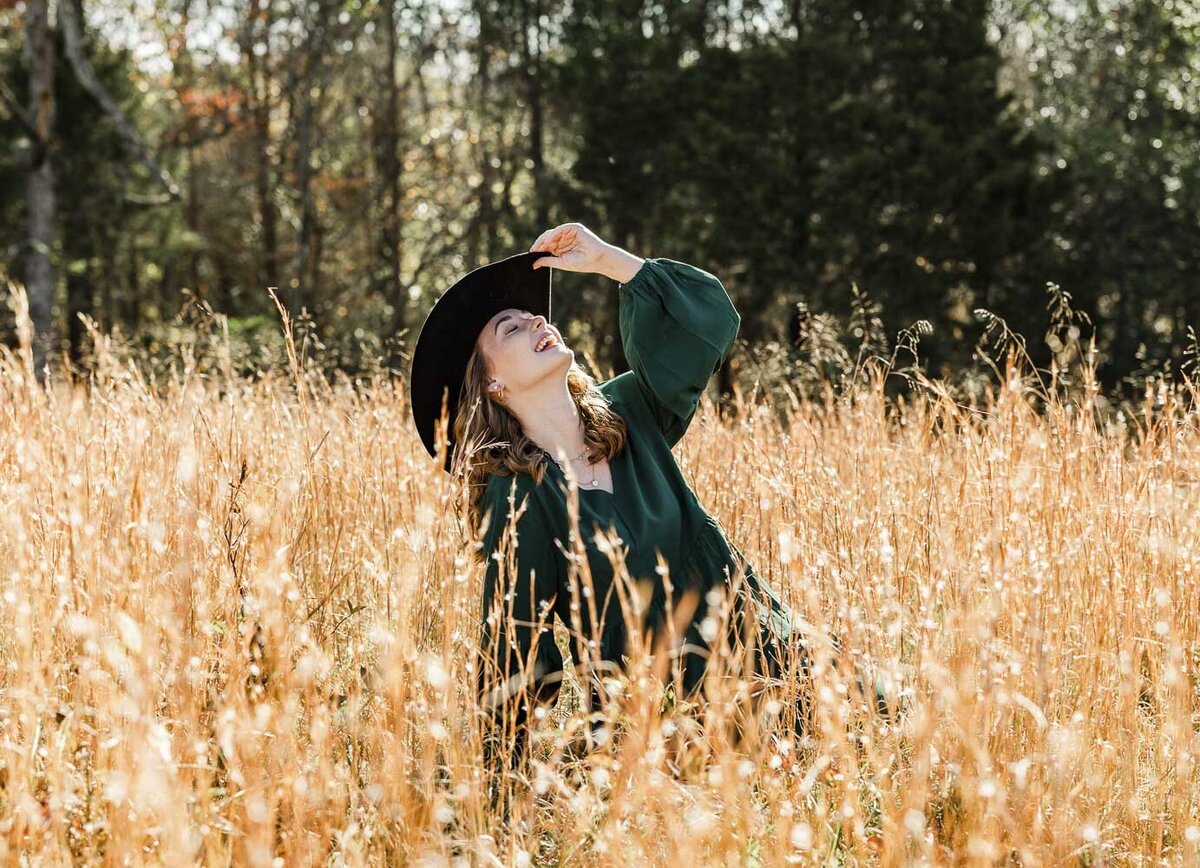 Girl playfully posing in an open field tipping her cowboy hat up