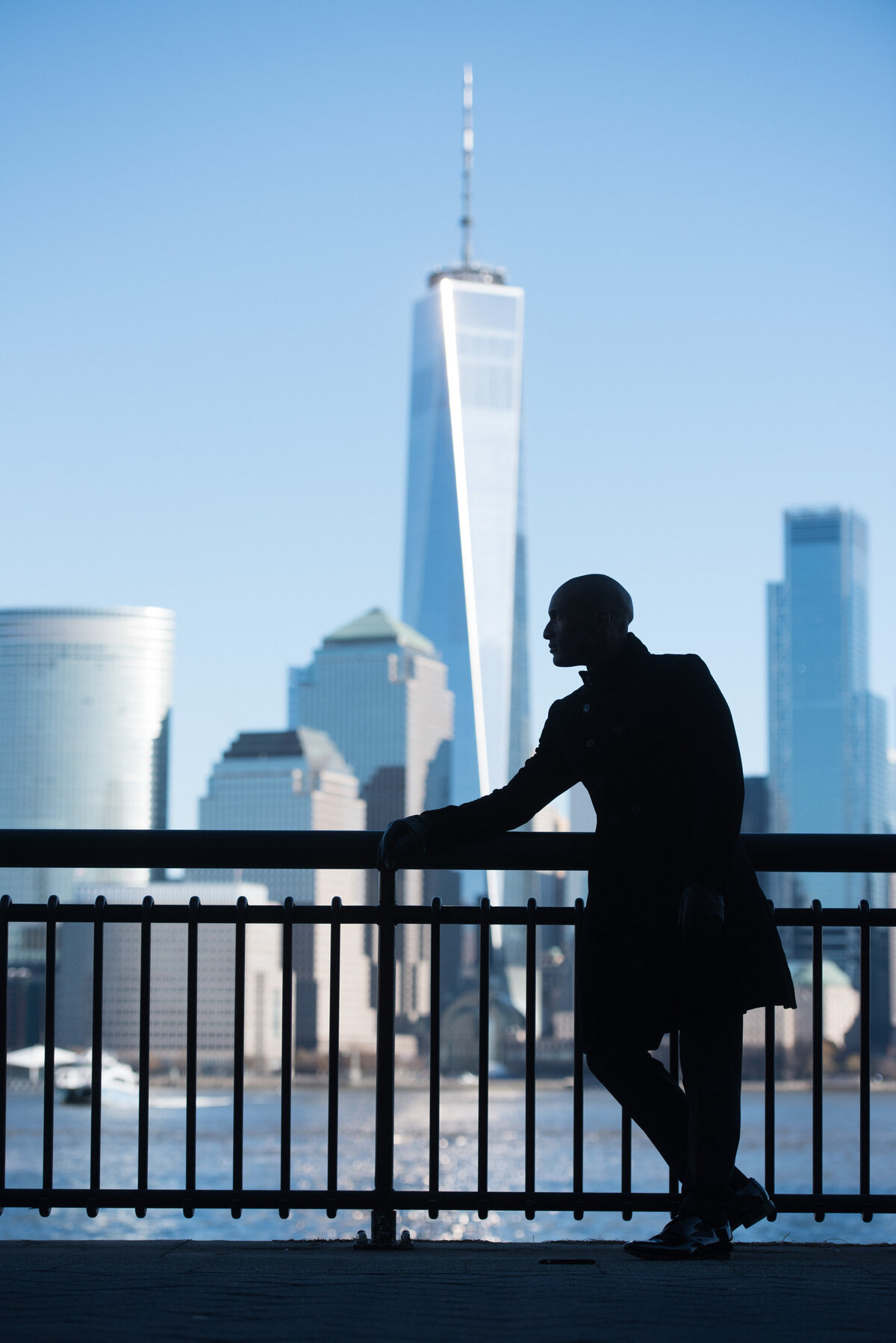 The silhouette of a person leaning against a railing with a city skyline behind him.