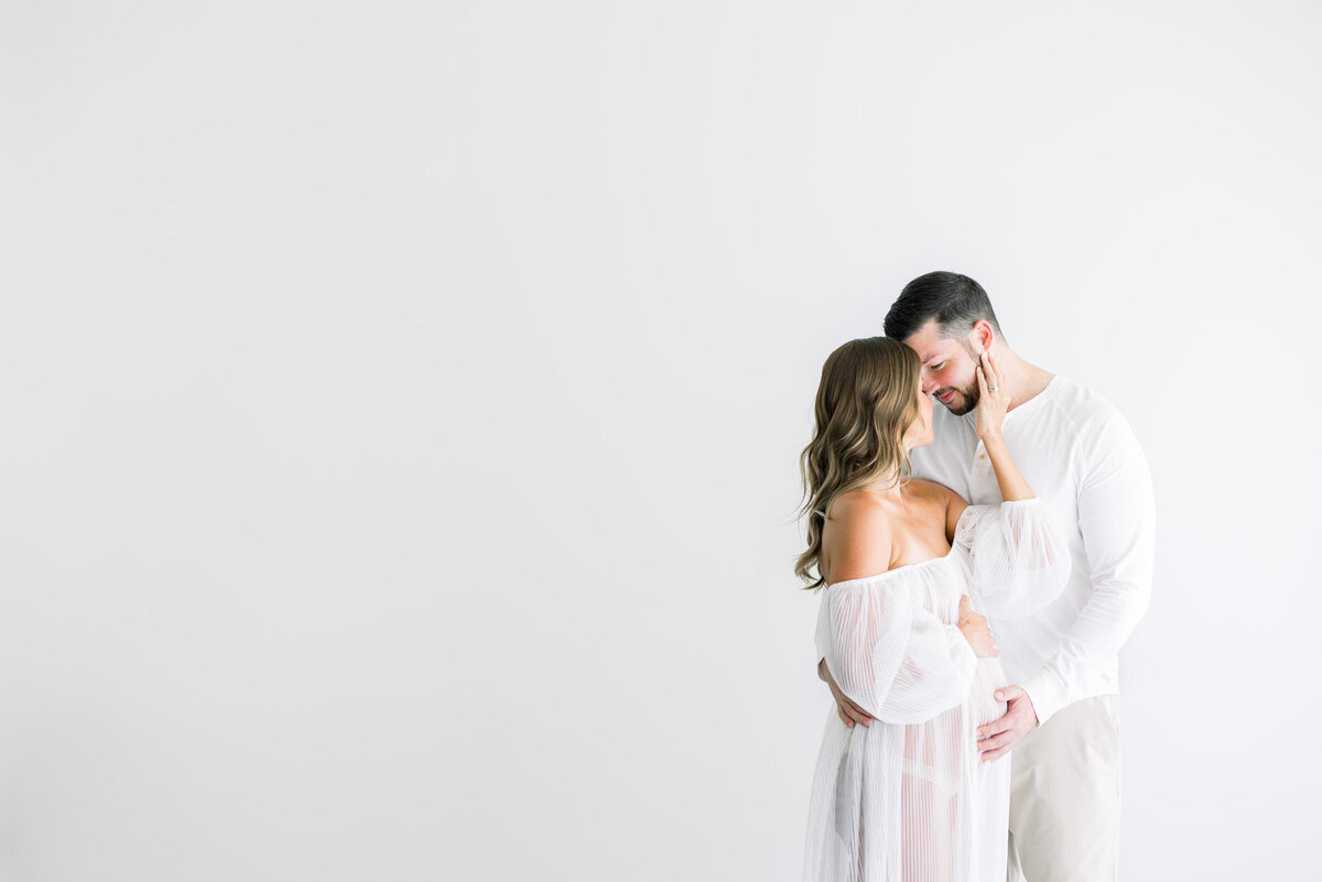 Husband with hand on pregnant belly of wife in white dress for Tampa maternity photographer Tina Marie Studio.