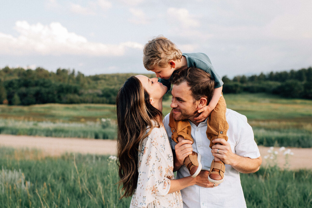 boy on dad's shoulders and boy leans down to kiss mom near denver