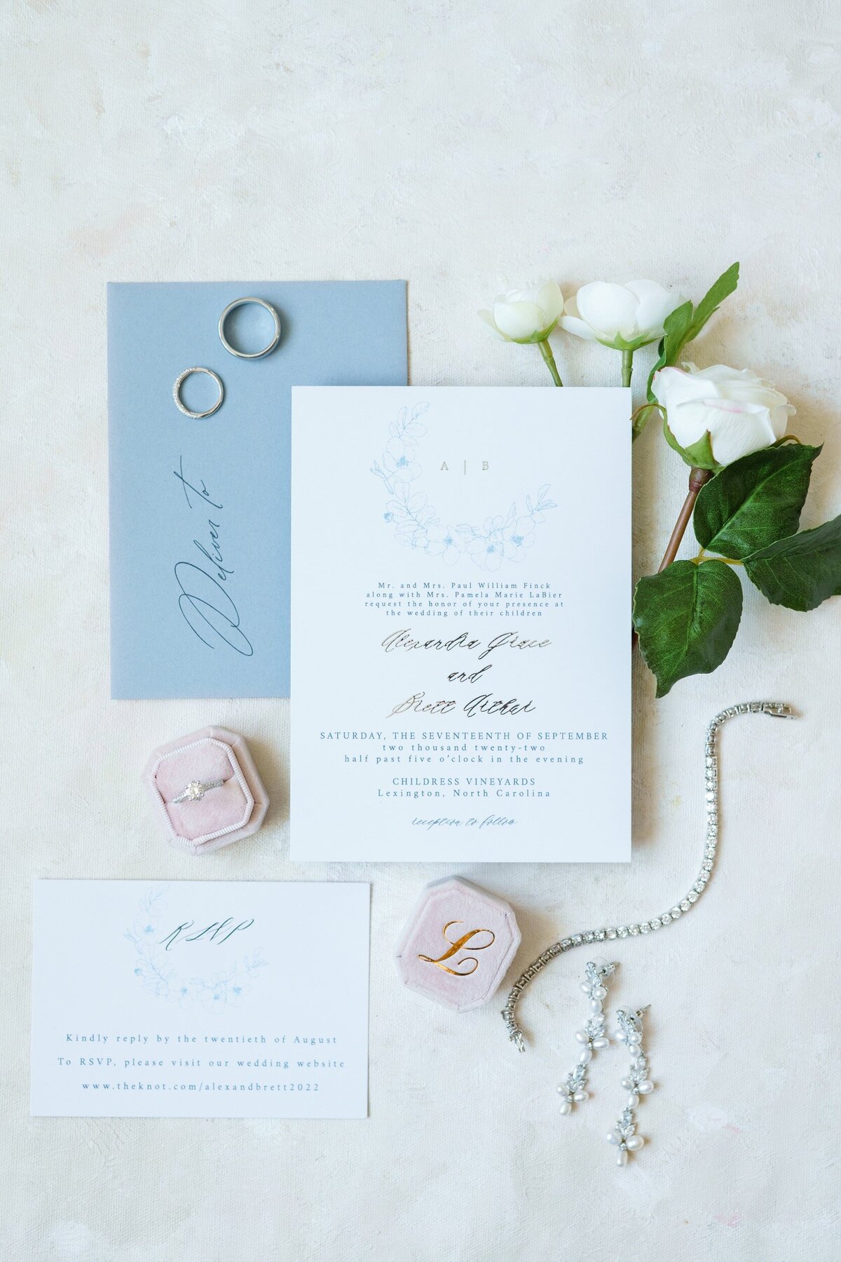 A flat lay of an invitation suite, jewelry, and a custom velvet ring box at a Charlotte, NC wedding.