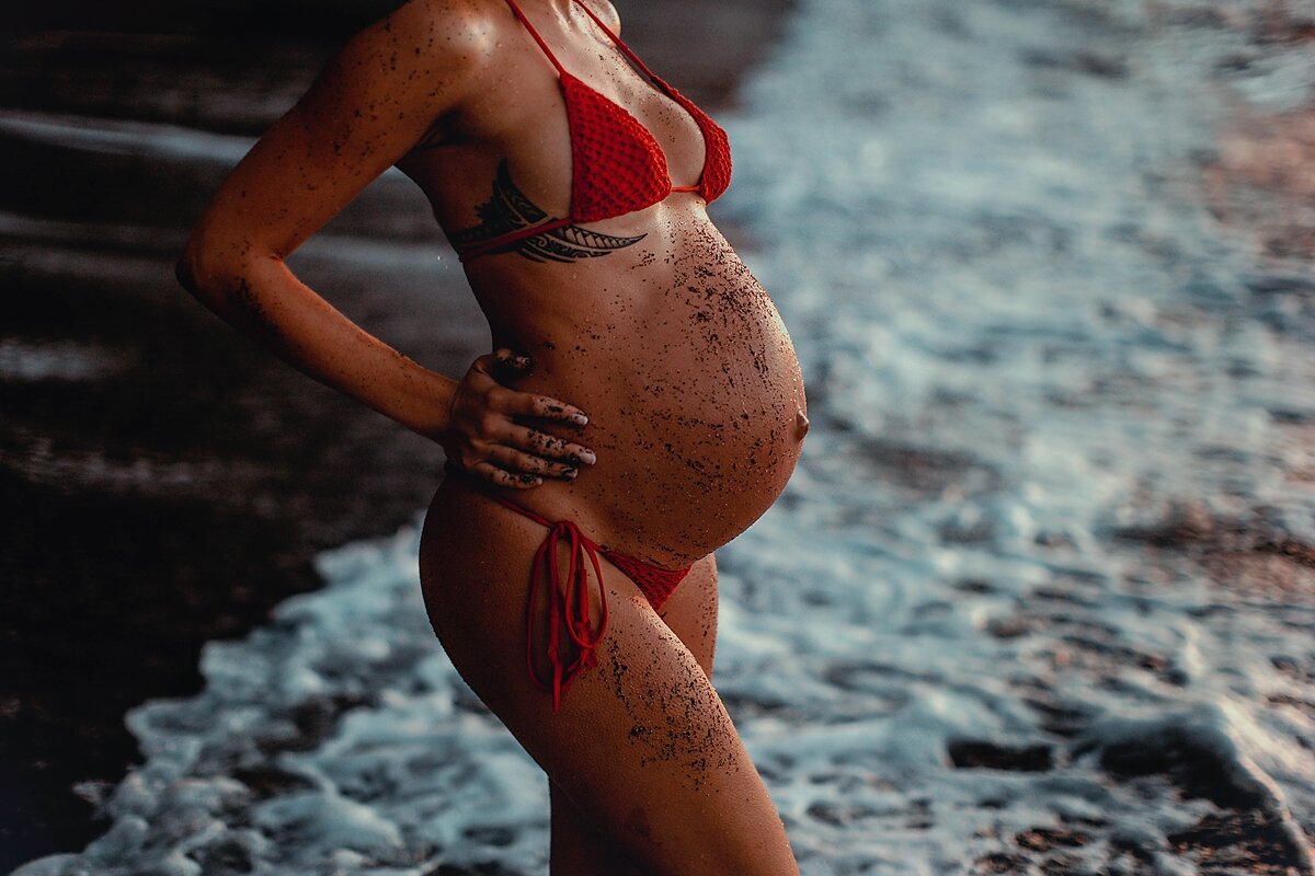 Black sand covers the belly of a tanned pregnant woman photographed in Makena on the island of Maui
