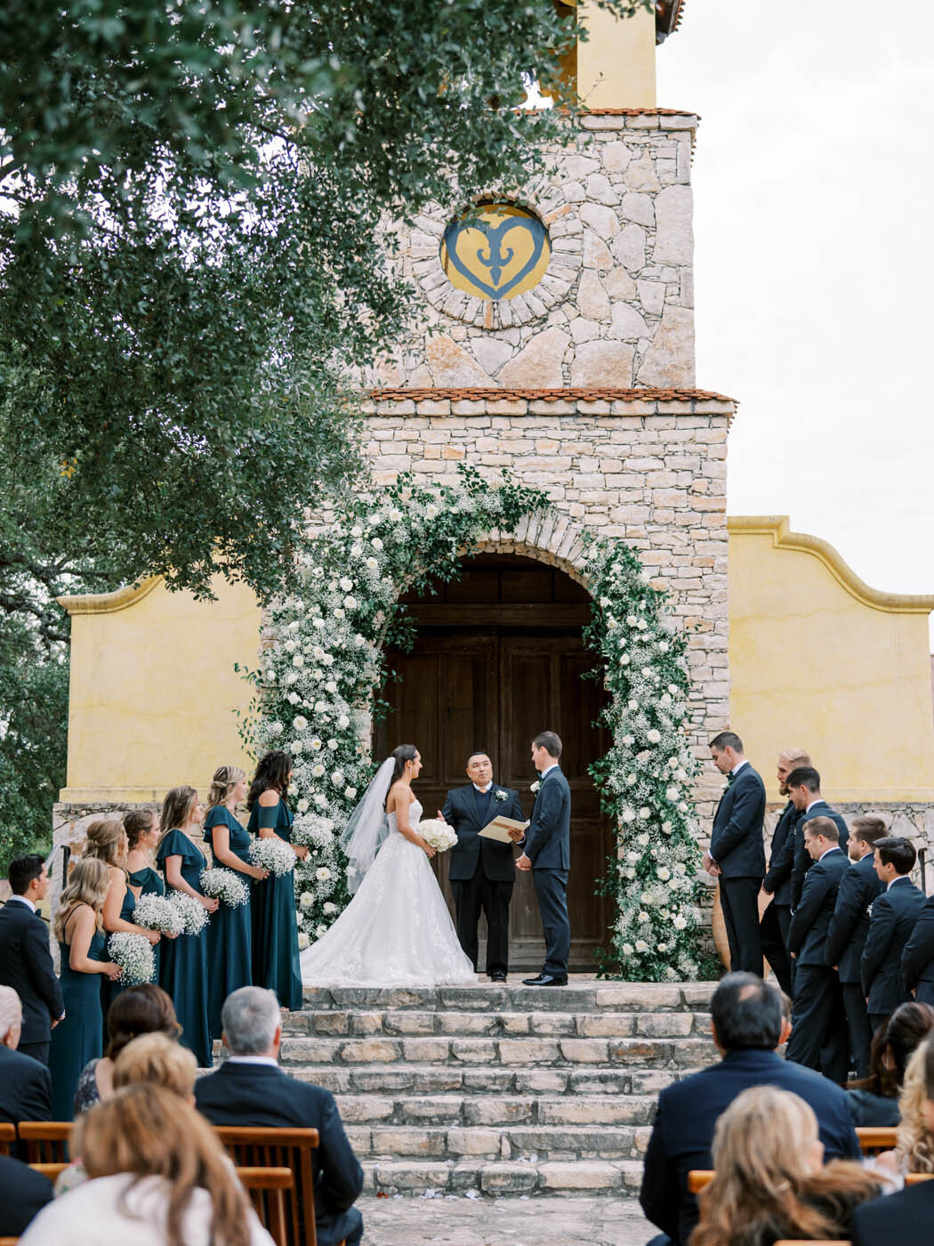 a ceremony on the stairs of ian's chapel with a green and white floral arch