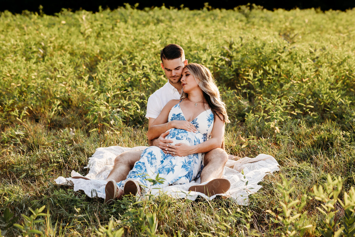 pregnant mother and husband laying on blanket in field by harrisburg pa maternity photographer