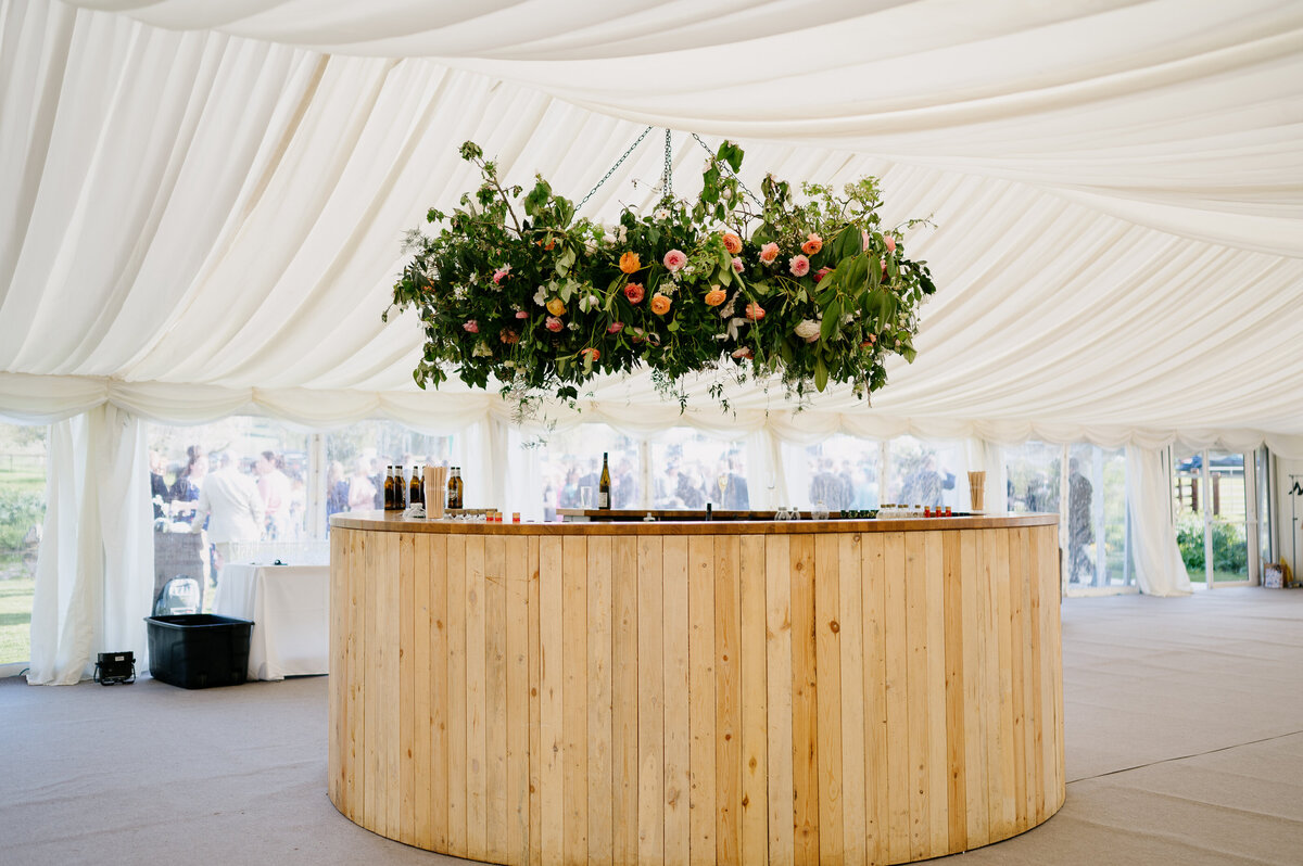 Suspended hoop of flowers above the round bar in the white marquee
