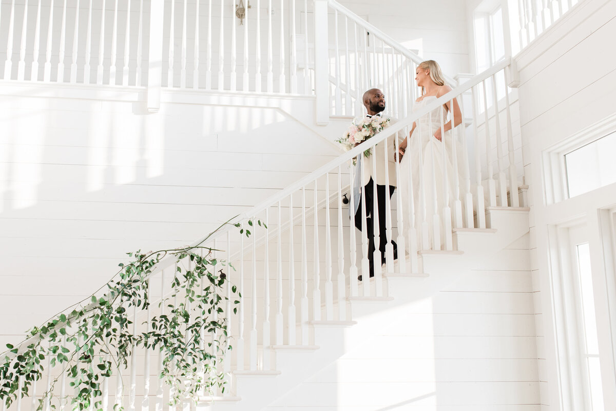 Groom guides his bride down a white staircase decorated with vines