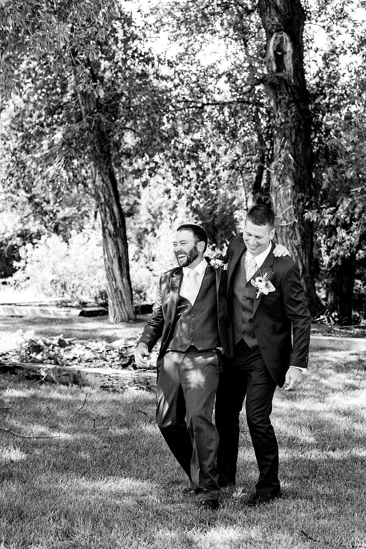 Black and white photo of groom laughing with one of his groomsmen while walking through the park