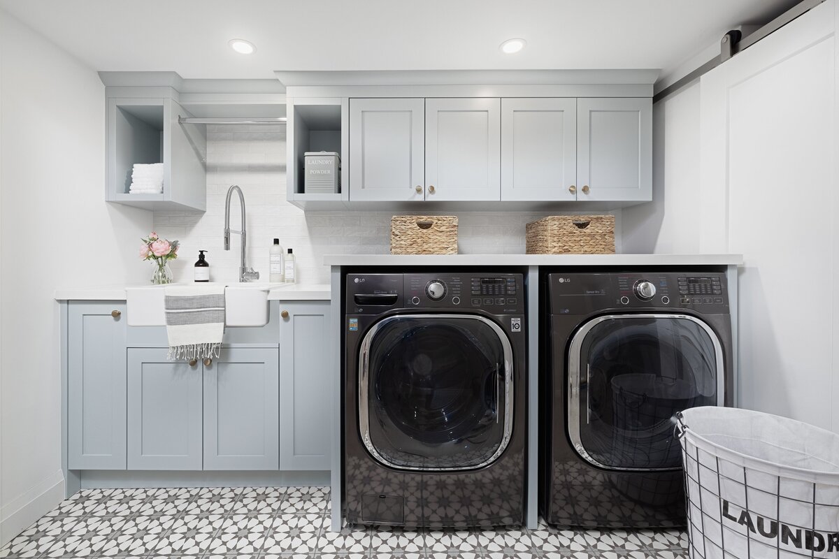 Laundry room with fun black and white tiles with a star pattern, soft blue cabinets, a farmhouse style sink, and a black washer and dryer