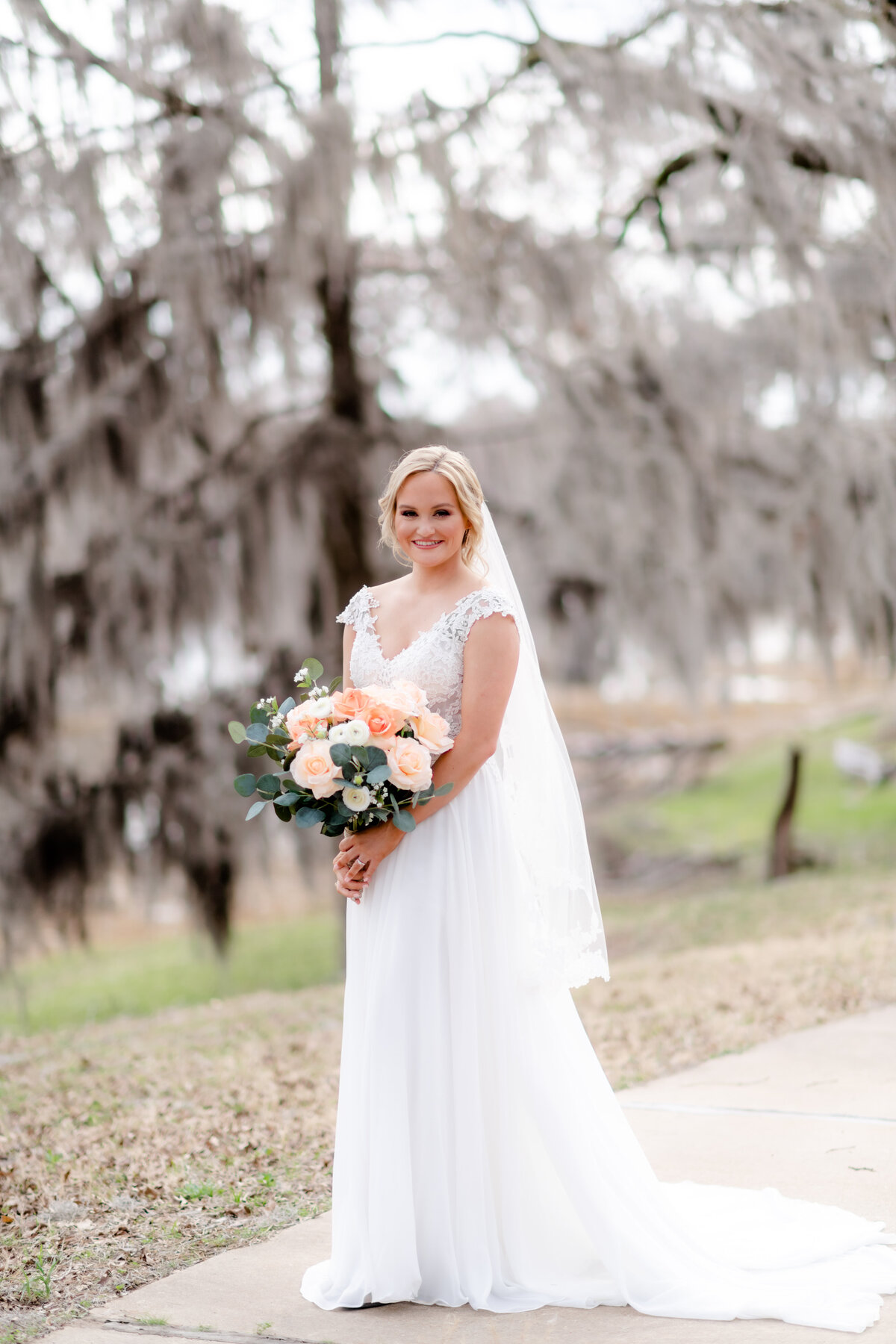 outdoor bridal session with blonde bride in a lace dress holding a coral wedding bouquet