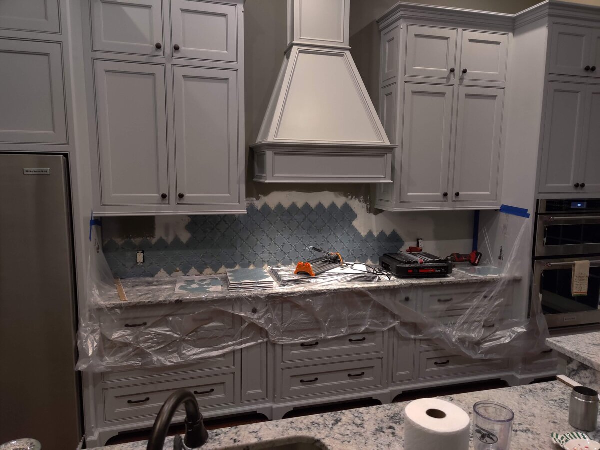 Grey kitchen cabinets and blue tile backsplash getting installed