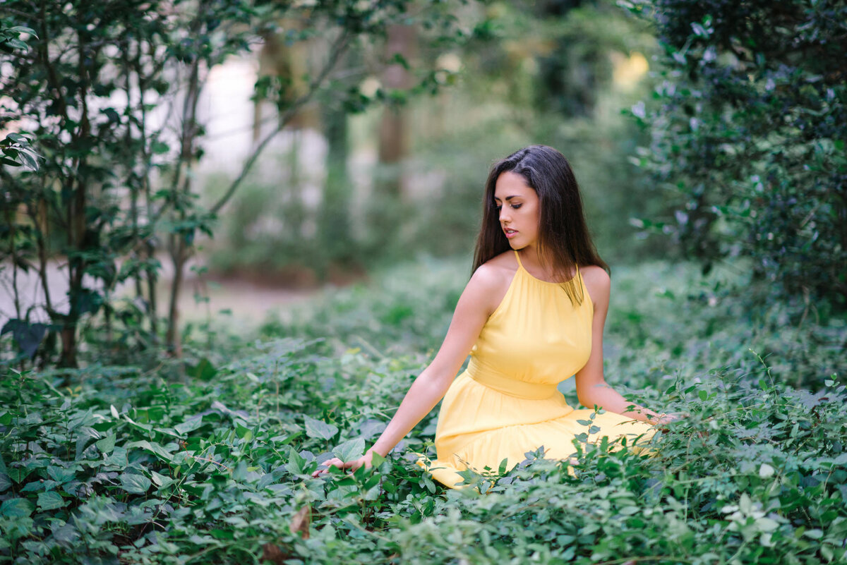 Senior girl in yellow dress surrounded by lush greenery in forest setting in Charleston, SC