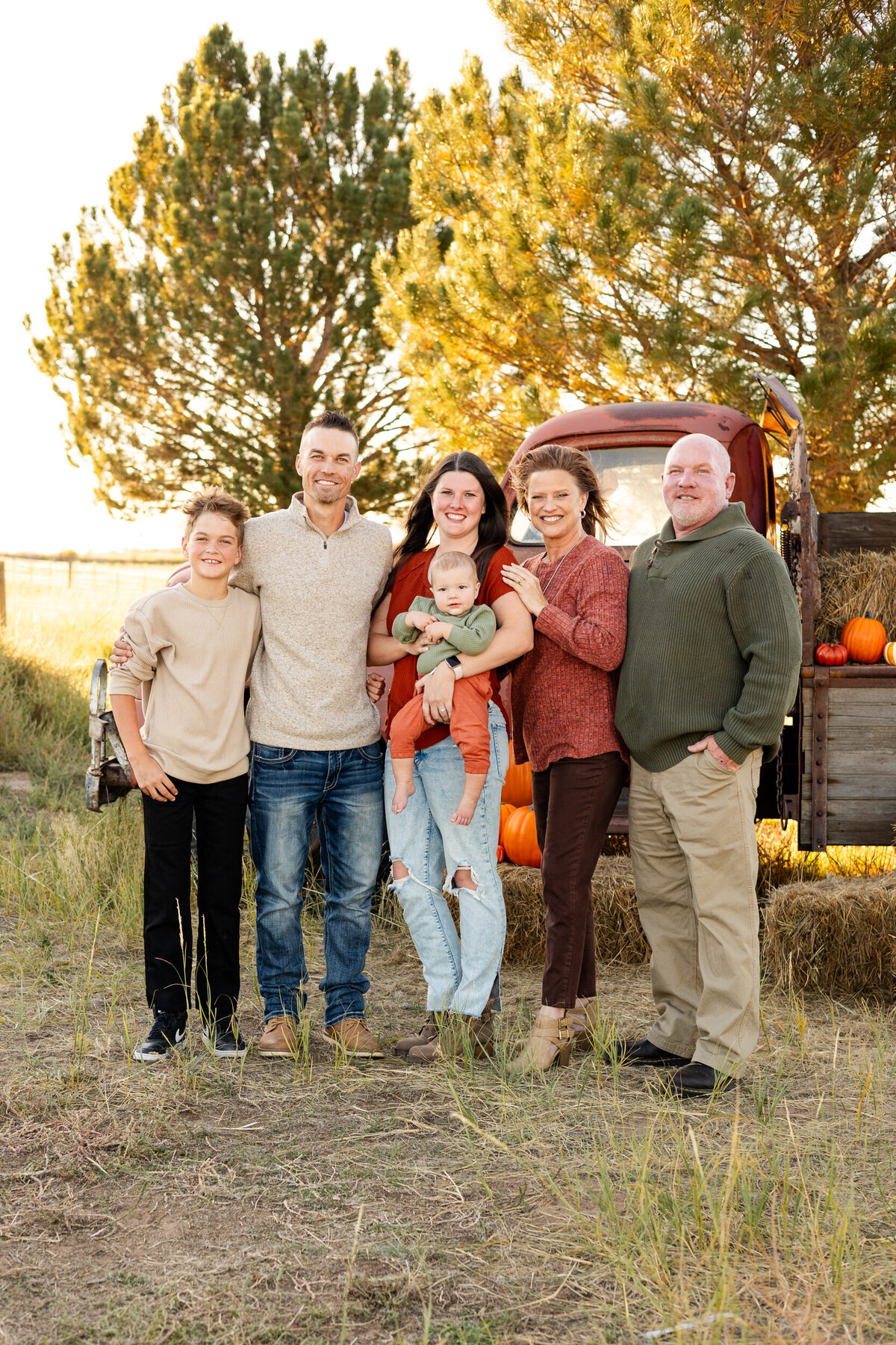Multigenerational family stands in front of a vintage red farm truck and smiles at the camera.