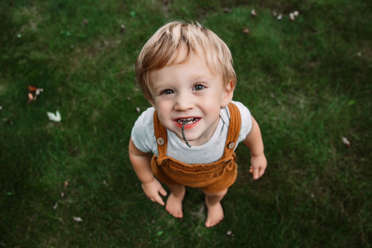 toddler stares up at camera with twig in mouth