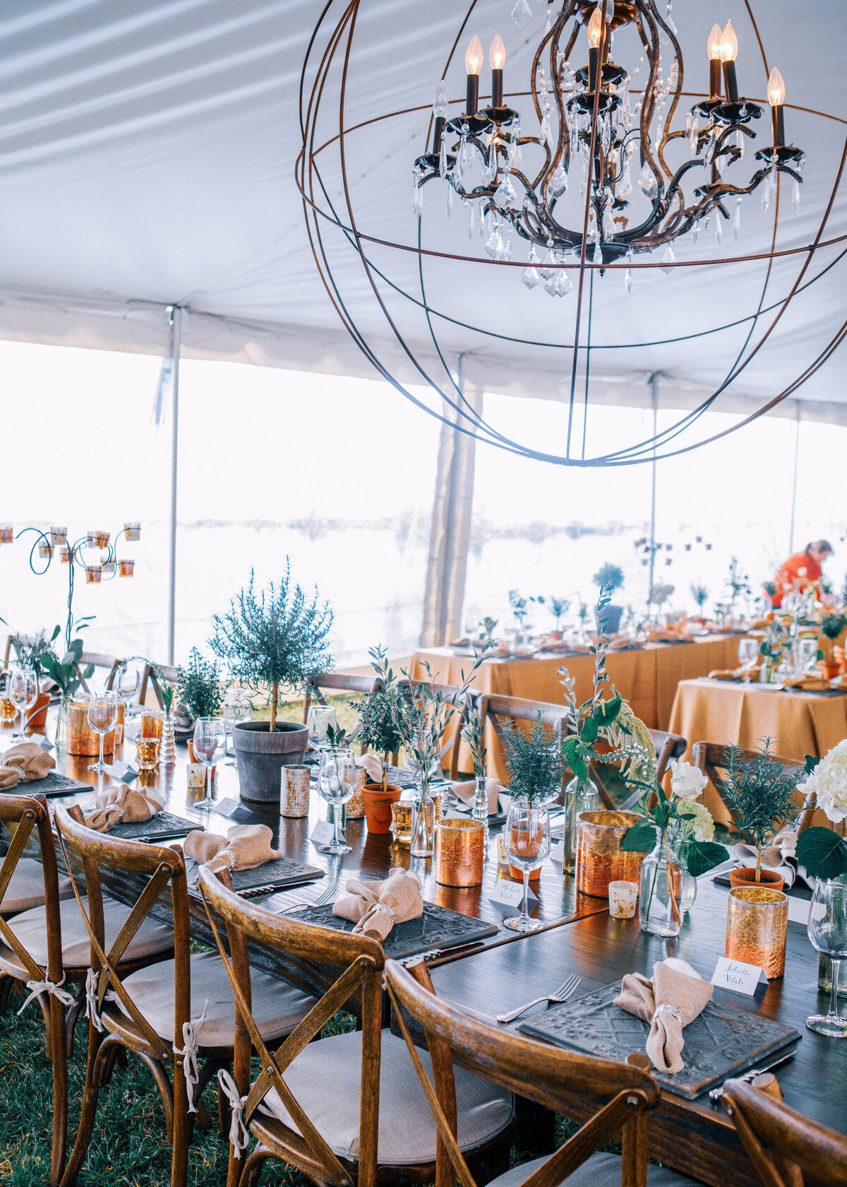 A rustic wedding in a marquee with a large round light chandelier and copper accents and wooden cross back chairs