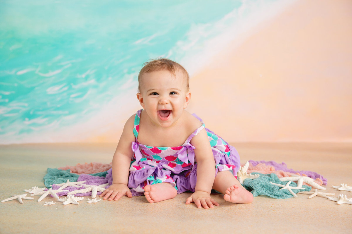 Baby girl smiles in a milestone portrait on a beach background in Myrtle Beach
