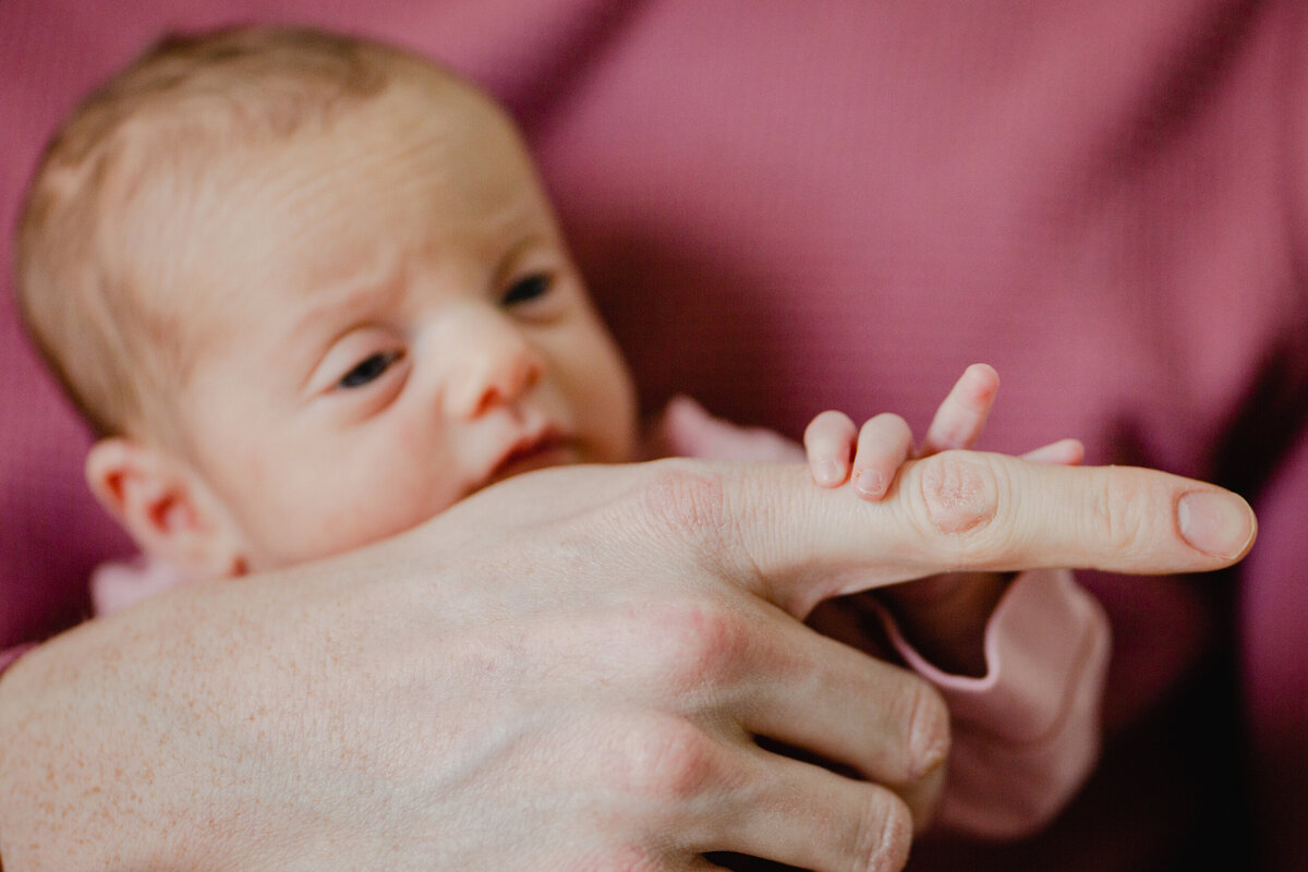 A three-week-old baby attempts to grip her dad's pointer finger.