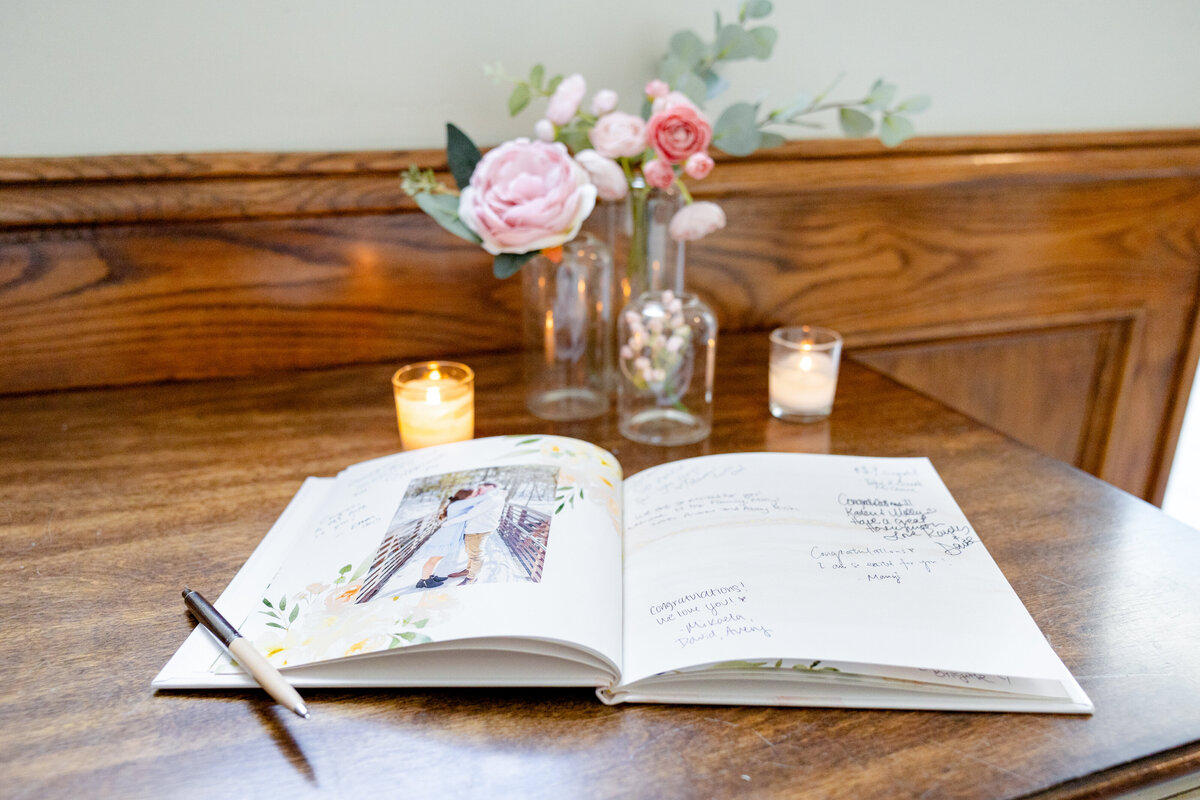 A wedding guestbook open on a wooden table, surrounded by floral centerpieces and glowing candles.