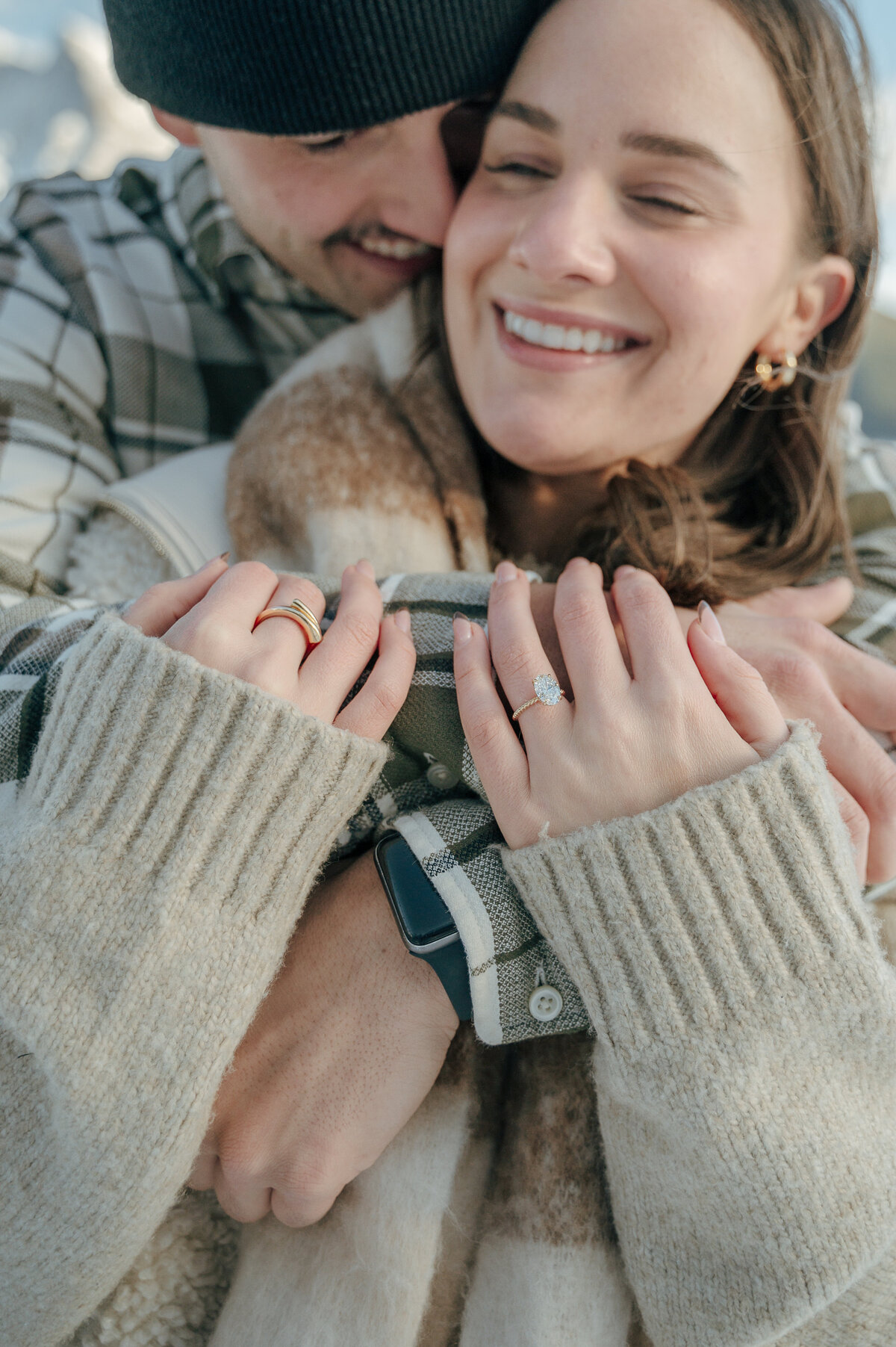 Candid moment of woman smiling as her partner hugs her tightly during an intimate and cozy engagement session in Banff.