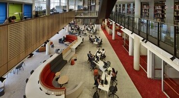 Spacious library interior at the University of Western Sydney Parramatta campus, showcasing a two-storey layout with open study areas and students walking through.